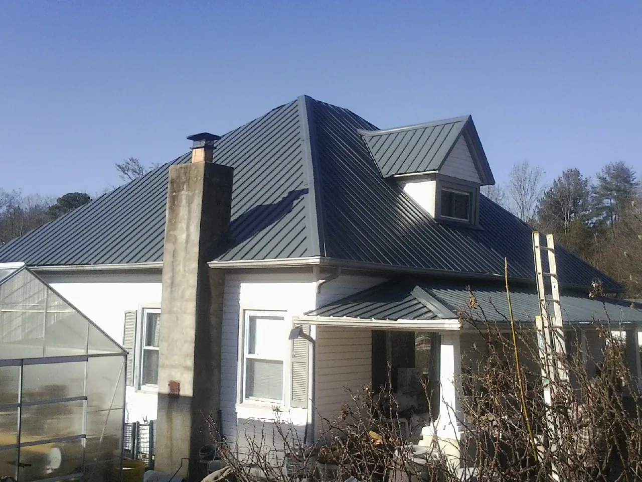 Dark blue standing seam metal roof on a white farmhouse with dormer — Slate & Tile Roof Repair by Roofing Brothers in Glenburn