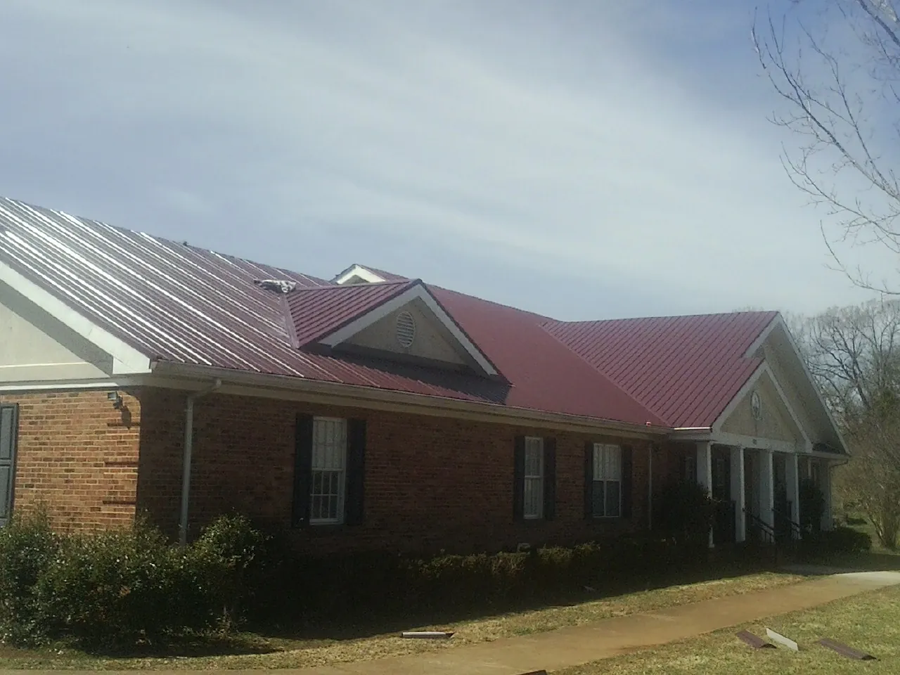 Red metal roof with gabled entries on a long brick building, from a Hail Damage Roof Repair job in Glenburn
