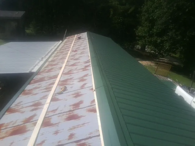 Old rusted panels beside newly installed green metal roofing — Wind Damage Roof Repair by Roofing Brothers in Glenburn