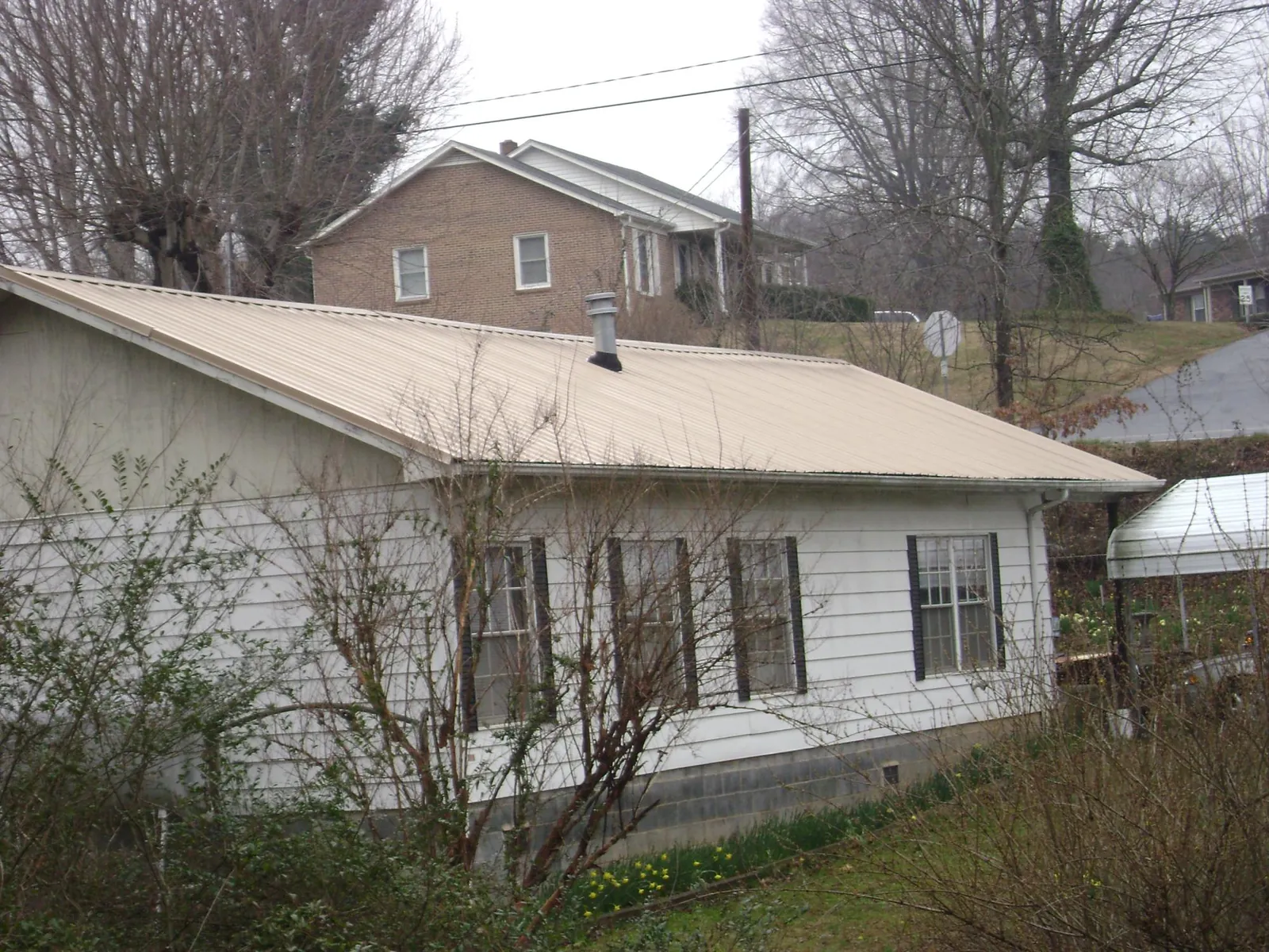 Tan metal roof on a white sided house set into a hillside — Commercial Roofing by Roofing Brothers in Glenburn